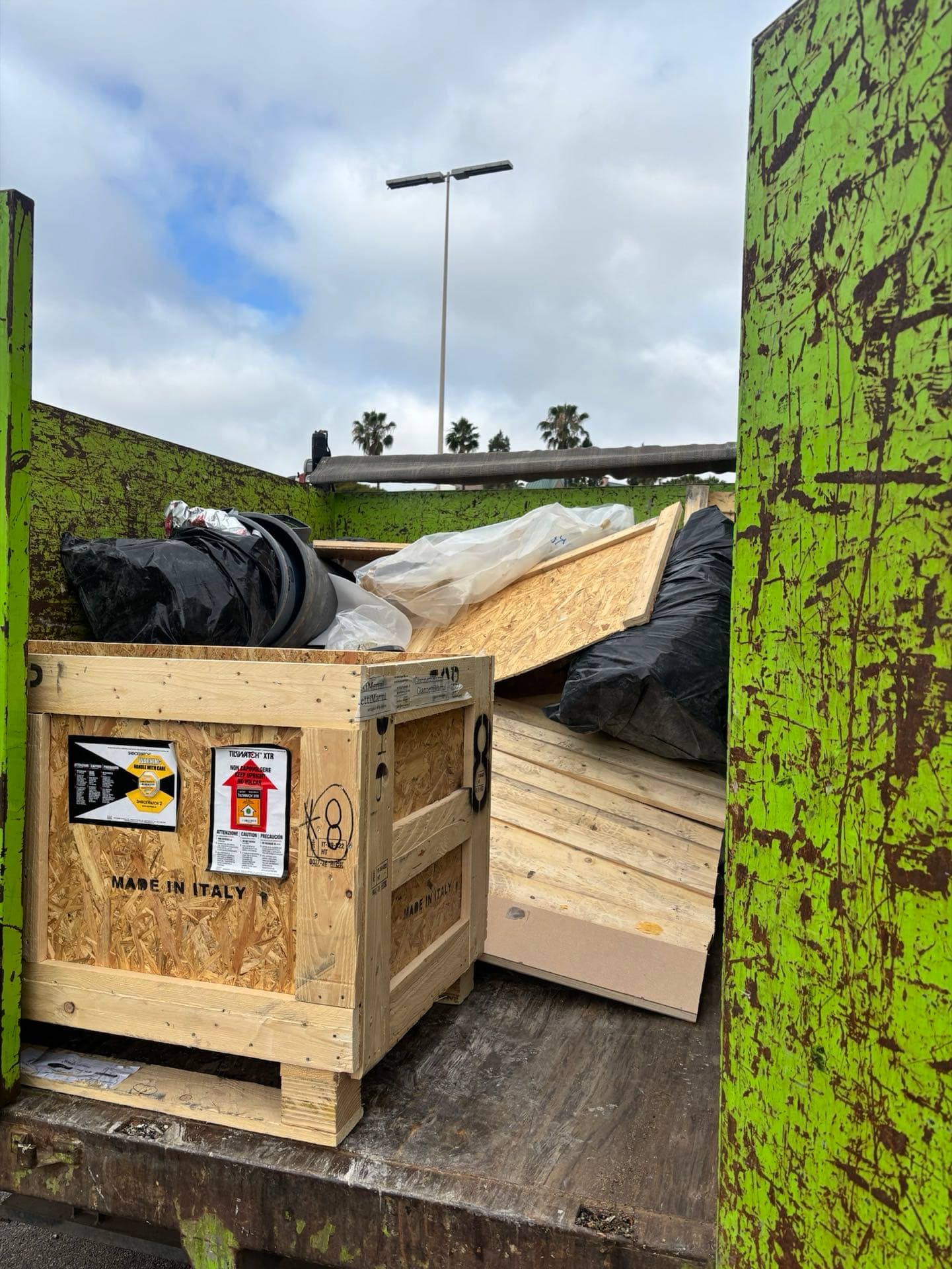 Outdoor crate and construction debris loaded for removal under San Diego palm trees
