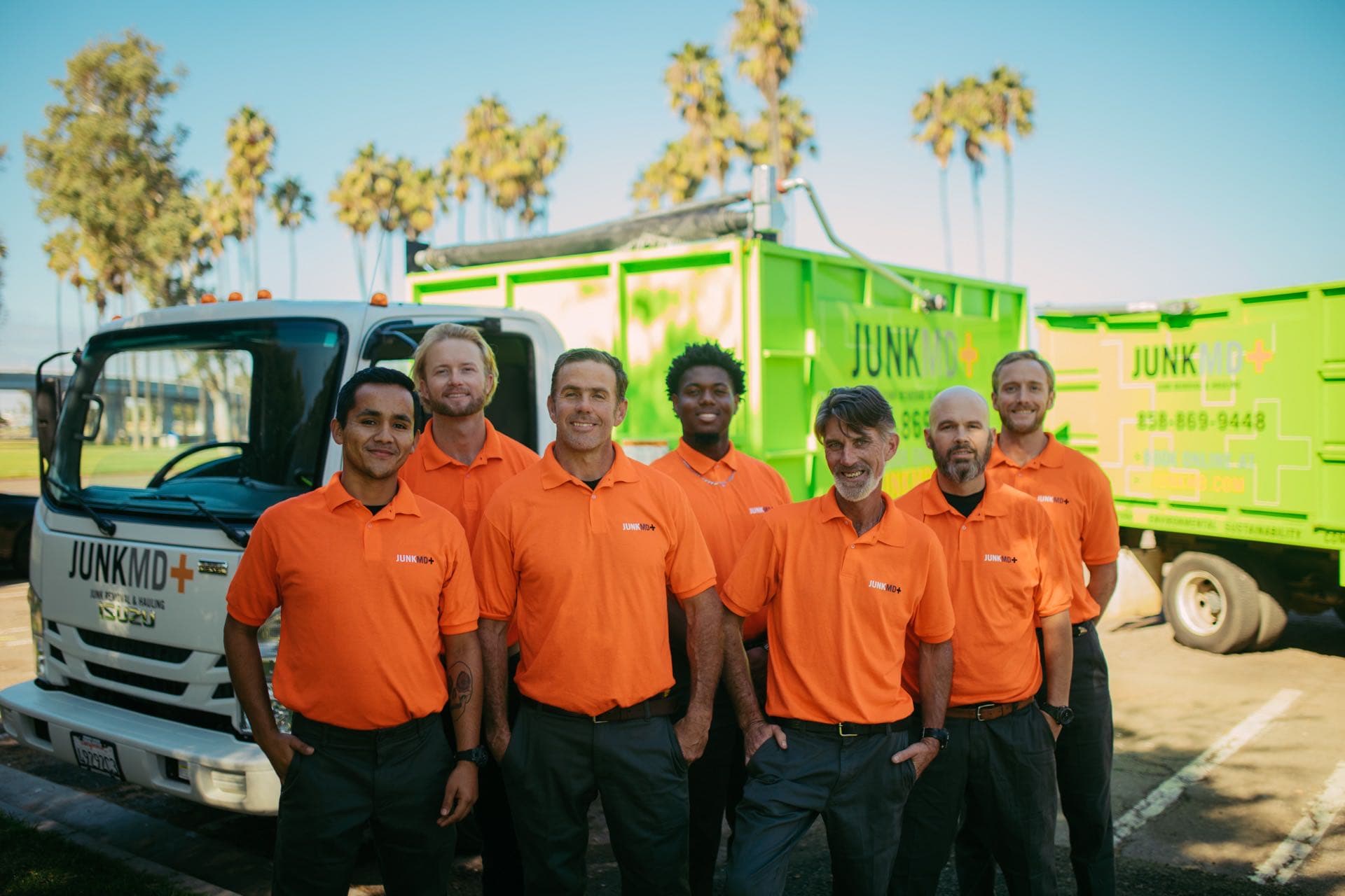 The full JunkMD+ crew lined up in front of two green junk-removal trucks in San Diego